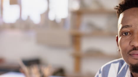 Half-face-of-african-american-man-with-beard-sitting-and-smiling-in-pottery-studio,-slow-motion