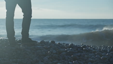 Seascape-close-up,-waves-crushing-at-black-pebbly-beach-when-man-walks-onto-it,-he-stops-and-picks-a-stone-to-throw-in-the-sea,-finally-he-leaves