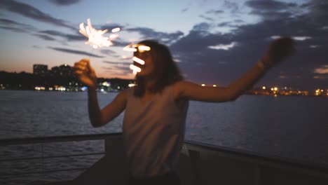 una joven hermosa baila en la cubierta de un barco con luces de bengala por la noche.