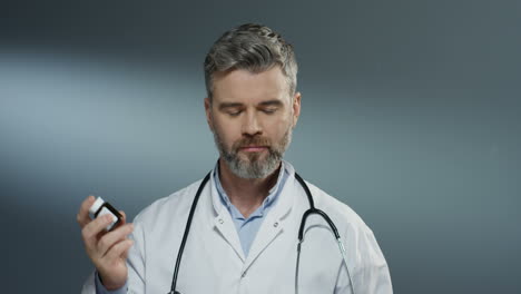 portrait shot of the man doctor shaking pills in bottle and the doing gesture like offering it to the viewer in camera