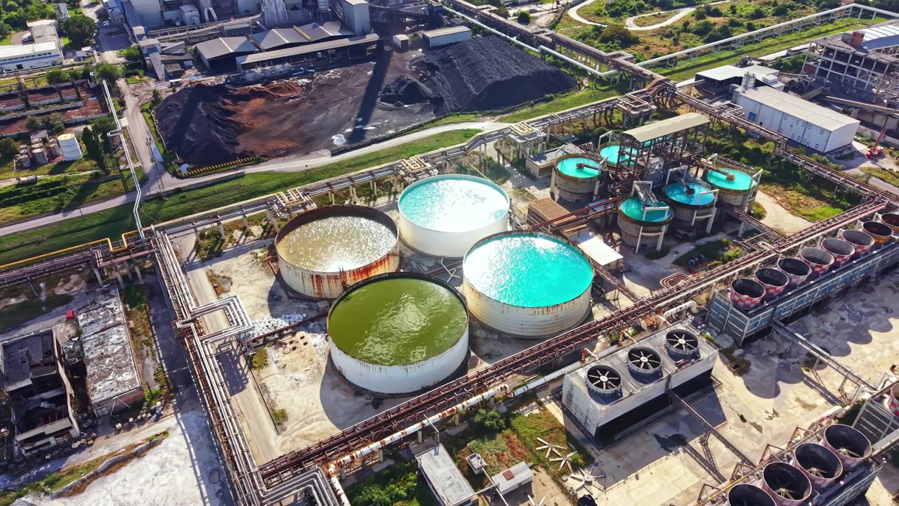 Wastewater treatment facility shown with several large tanks filled with different colored liquids located in an industrial area during the daytime