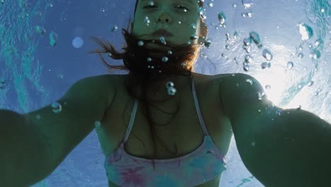 underwater selfie of beautiful cute little red-haired girl holding breath while floating in transparent sea water