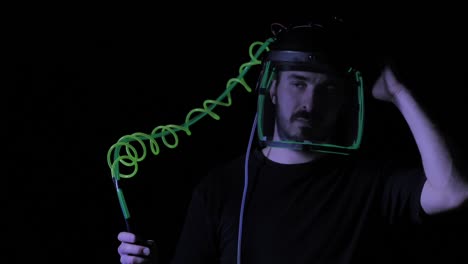 man wearing plastic face shield connected to coiled neon tube, closeup tilt up