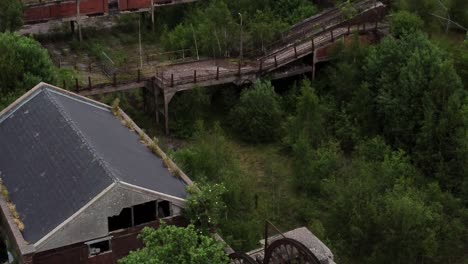 Abandoned-old-overgrown-coal-mine-industrial-rusting-pit-wheel-aerial-view-descending-reveal