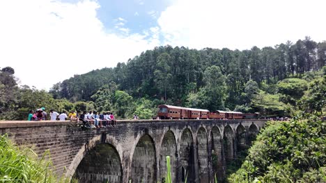 tourists leisurely sit on the historic nine arches bridge in sri lanka, surrounded by lush green forests. pan left