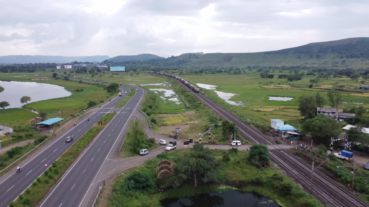 vista aérea de la vía férrea india y la autopista india que corren paralelas en una sola toma con el tren de carga y el paso de la locomotora