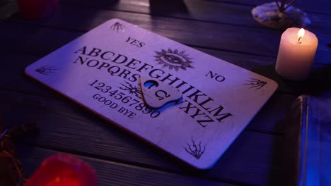 close up video of a wooden ouija board on a table surrounded by candles and a cross in a muffed - close up video of a wooden ouija board on a table. wax candles and a cross around. the planchette is slowly moving across the board, spelling out words and numbers. creative mystical content