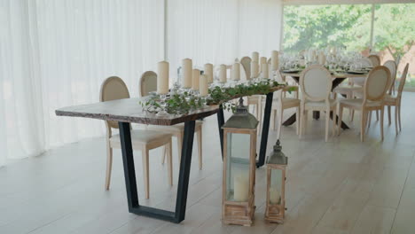 elegant dining setup with long wooden table, candles, and decorative lanterns in a bright, airy room