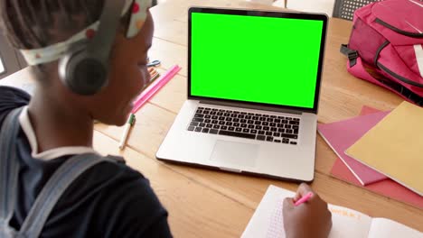 African-american-female-stundent-taking-notes-and-using-laptop-with-copy-space-on-screen