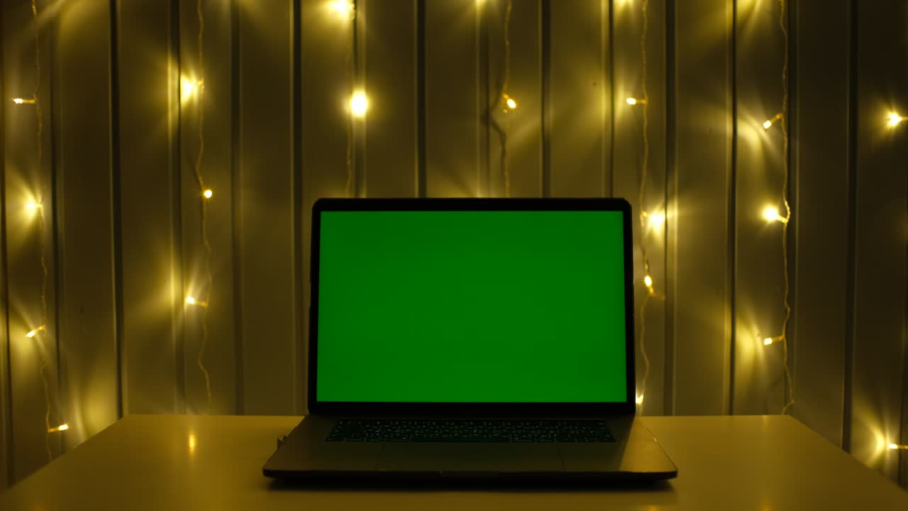 Green screen laptop computer on a homework desk in dark room with garland background