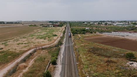 aerial footage flying backwards as a passenger train goes by on the tracks in bari, italy