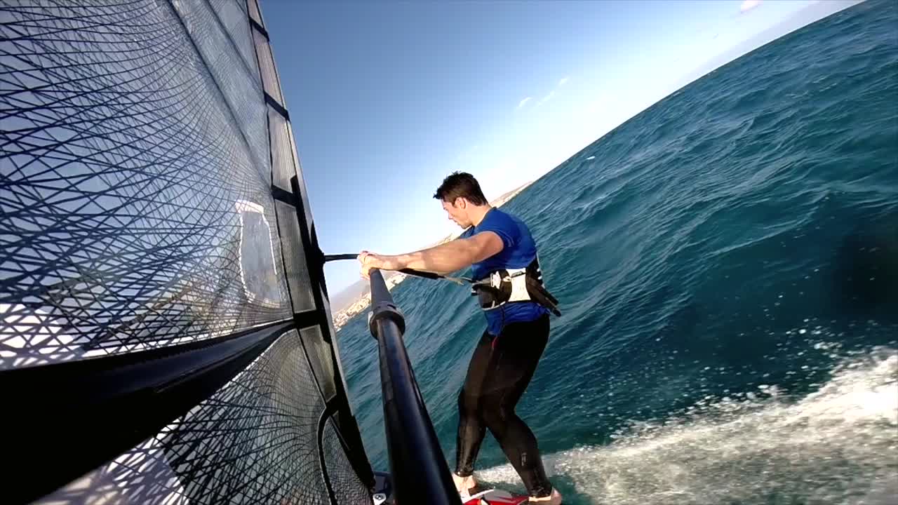 una vista trasera de un windsurfista en forma planeando a través del océano