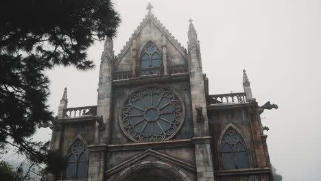 Alte-Gotische-Kathedrale-Mit-Großen-Fenstern-Und-Einer-Windmühle,-Die-Im-Nebel-Steht,-Umgeben-Von-Grünen-Wäldern-Vor-Einem-Gewitter