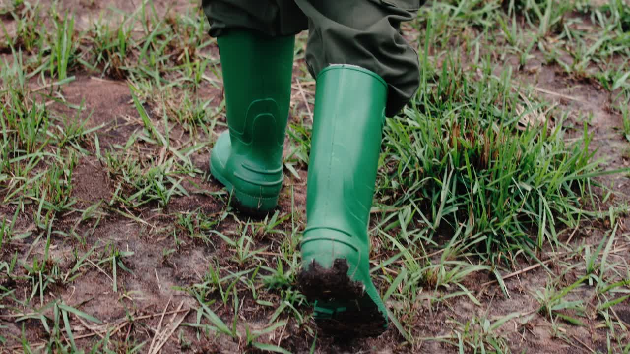 persona camina sobre un paisaje fangoso con botas de lluvia verdes