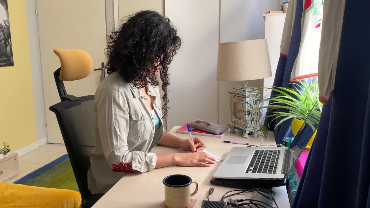 una giovane bella ragazza persiana donna iraniana stanno lavorando a casa in iran teheran usando laptop e quaderno per scrivere con penna colore giallo home design scrivania e la pianta naturale all'interno di casa portatile stand