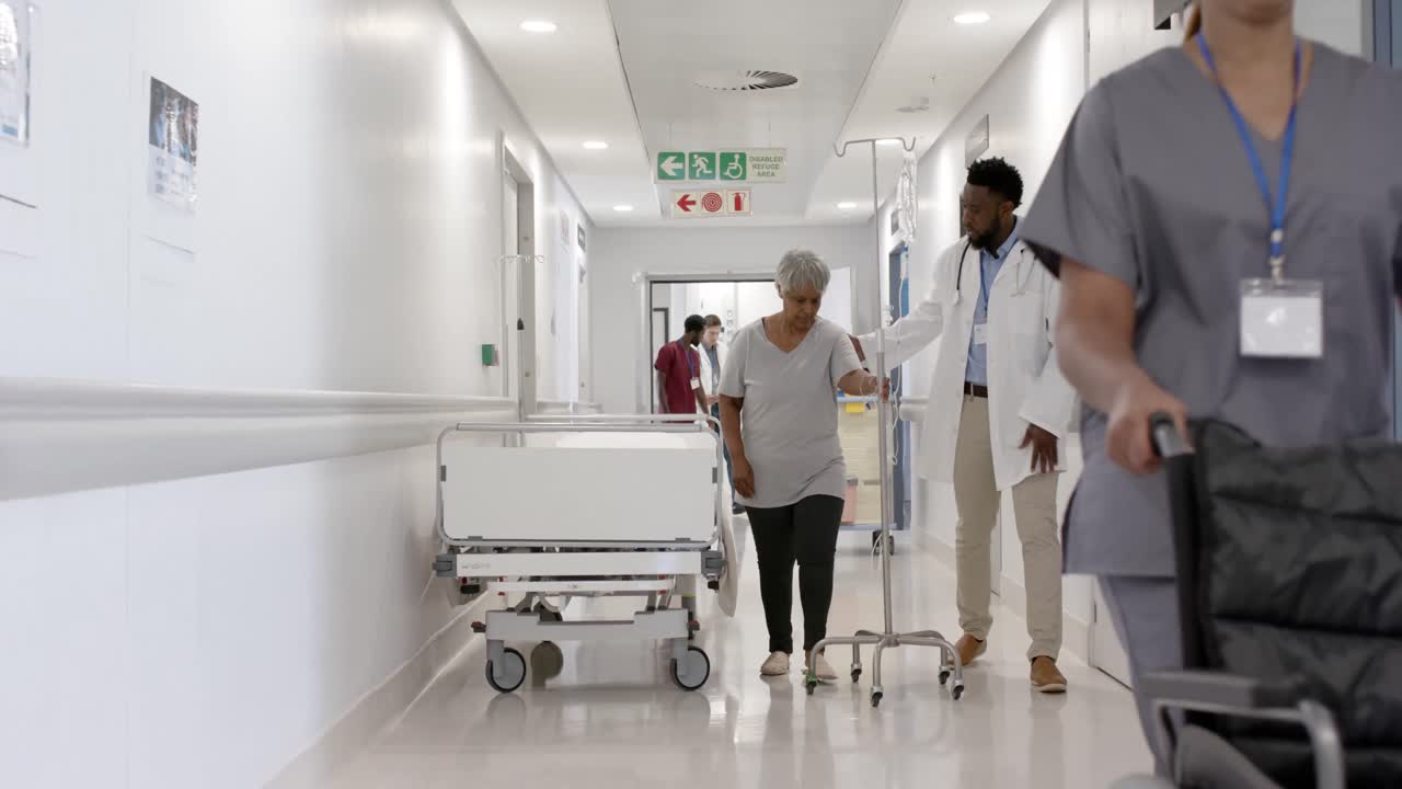 Ciddi, farklı etnik kökenli erkek doktor, serum takılı yürüyen yaşlı hastayla yavaş çekimde konuşuyor, değiştirilmemiş.