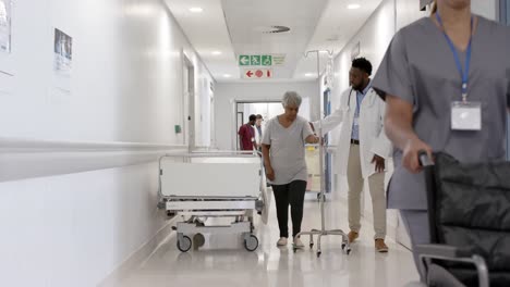 serious diverse male doctor talking to senior patient with drip walking in slow motion, unaltered