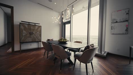 push in shot of a large dining room table set up in a high rise condominium next to large windows letting in natural sunlight