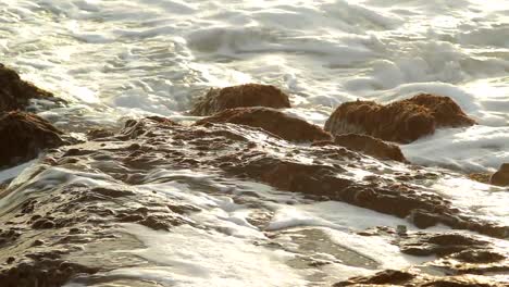 sea waves splashing on rocks at the beach during sunset