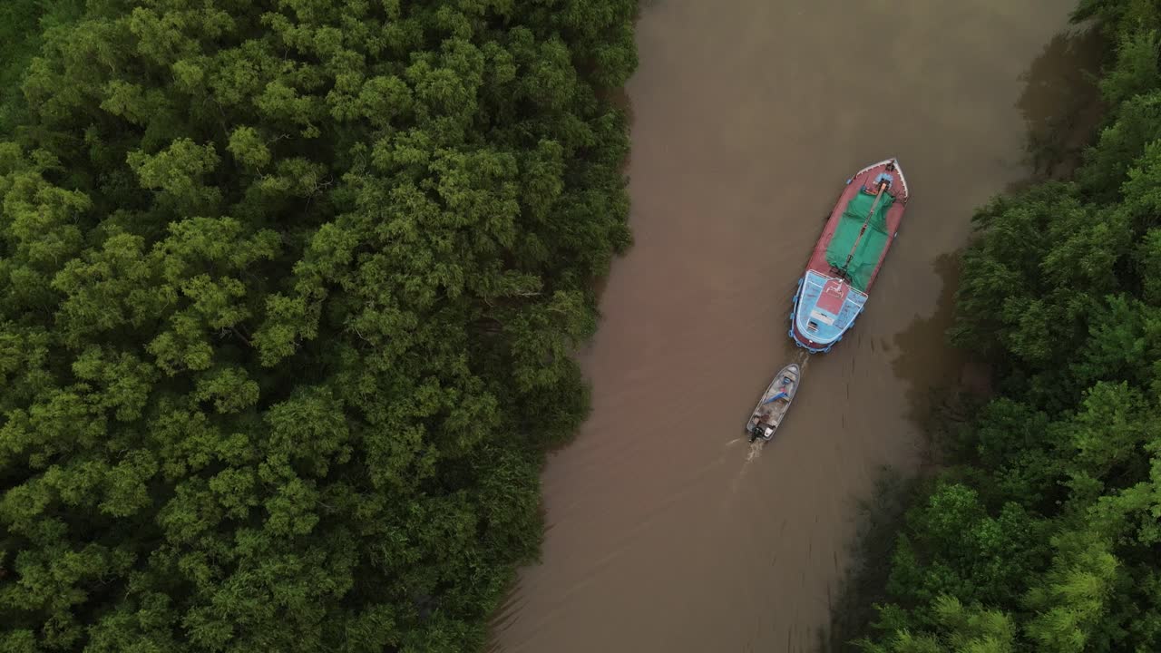 dron cinemático de arriba hacia abajo de un barco que transportaba un bote pequeño en el río amazonas rodeado de árboles verdes de la selva tropical durante la puesta de sol