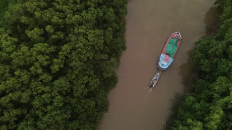 cinematic drone top down shot of ship carrying small boat on amazon river surrounded by green rainforest trees during sunset