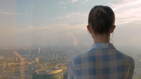 woman looking at cityscape through window of skyscraper - back view