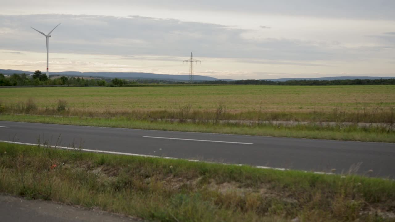 풍력 터빈과 배경에서 열린 필드와 함께 속도를 내는 흐릿한 자동차, 황혼에