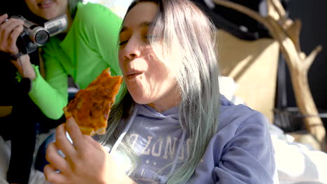 close up of a girl eating pizza at home while her friend recording a video