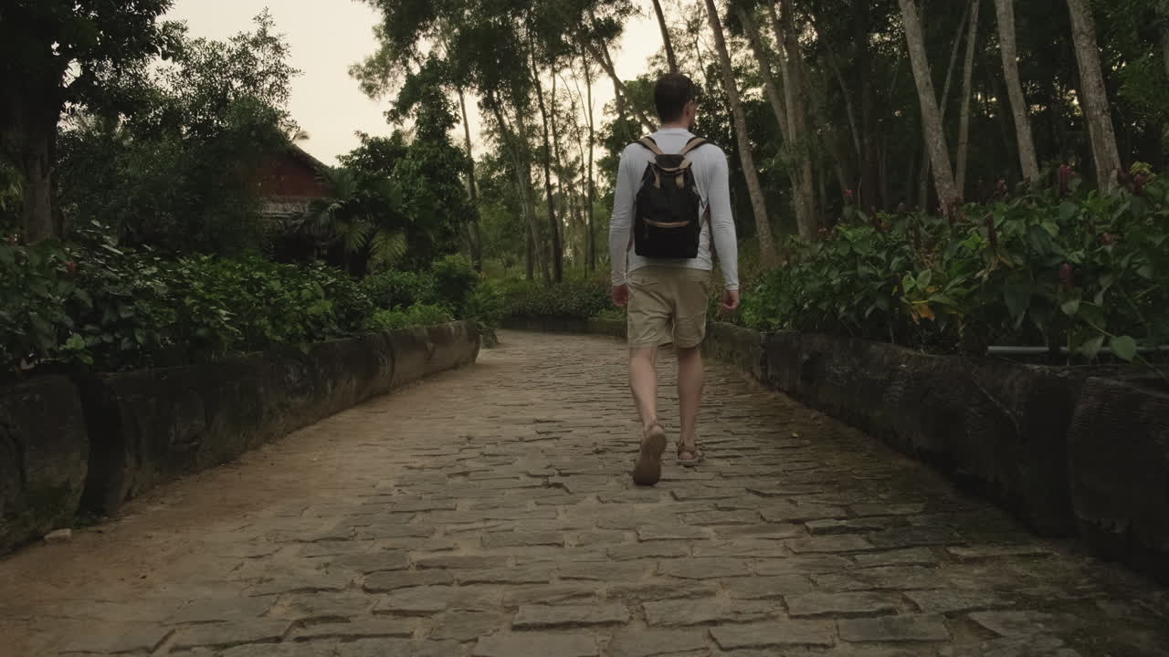 hombre caminando por un camino de piedra en un jardín tropical