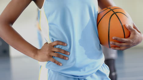 holding basketball, female athlete standing confidently on school court
