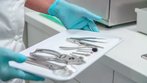 Medical-professional-holding-instruments-on-tray-wearing-blue-latex-gloves