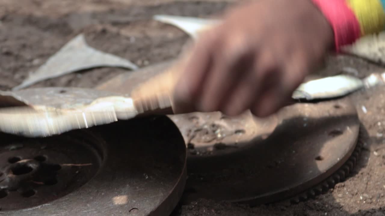 Primo piano di un adolescente congolese che raddrizza un pezzo d'auto per la produzione di stufe a carbone