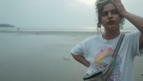 young indian woman gracefully gazing at camera while it zooms in on cloudy beach day