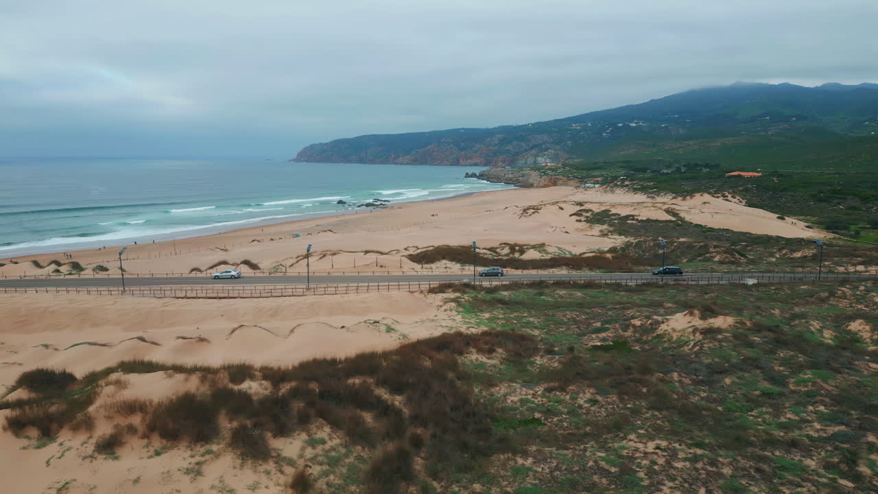 Foamy waves washing beach lined with sandy dunes drone view. Road stretching