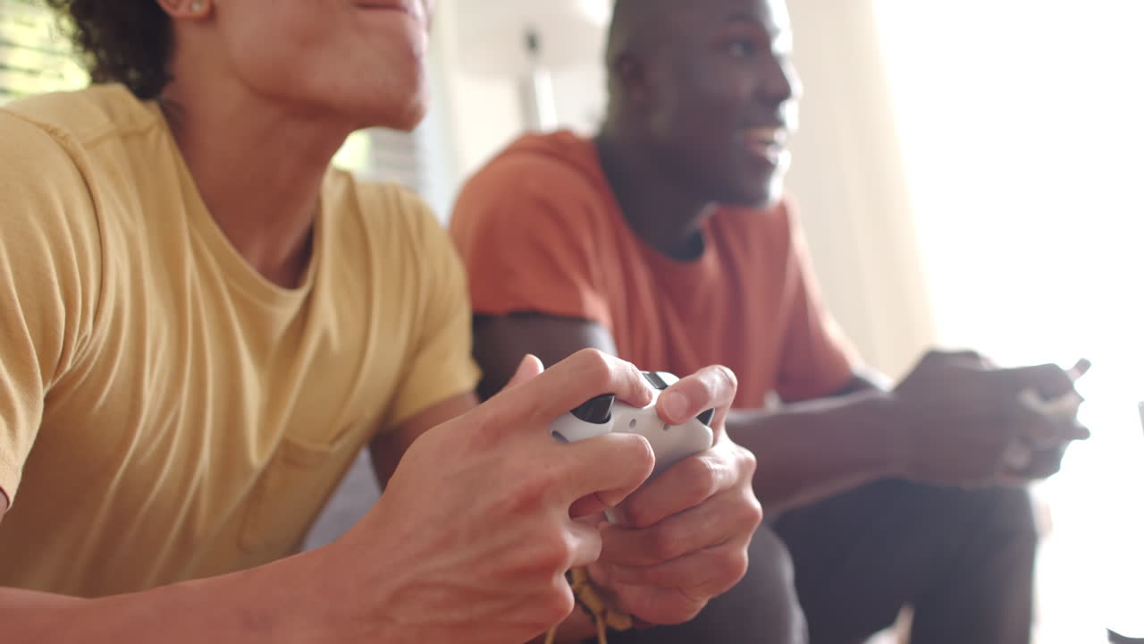 Due amici maschi multirazziali giocano ai videogiochi, godendosi il tempo insieme sul divano di casa