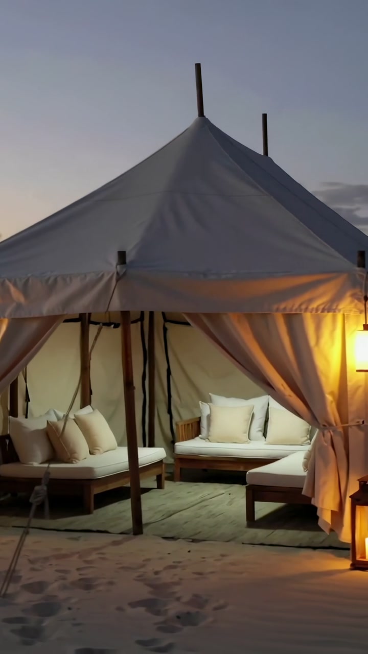 Vertical video: Panning camera revealing canvas tent on shore at dusk, showing beds, lamp for rest