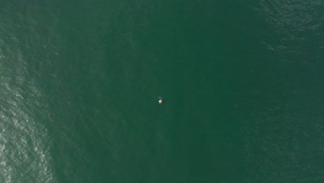 a solitary fisherman floats on an inner tube in the vast expanse of the moroccan ocean, casting his line into the deep blue waters