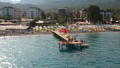 Aerial-drone-shot-of-people-swimming-and-sunbathing-on-a-pier-at-a-hotel-beach-in-Kemer,-Turkey