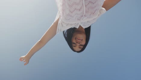 happy hispanic woman dancing with arms outstretched on sunny beach, smiling, slow motion