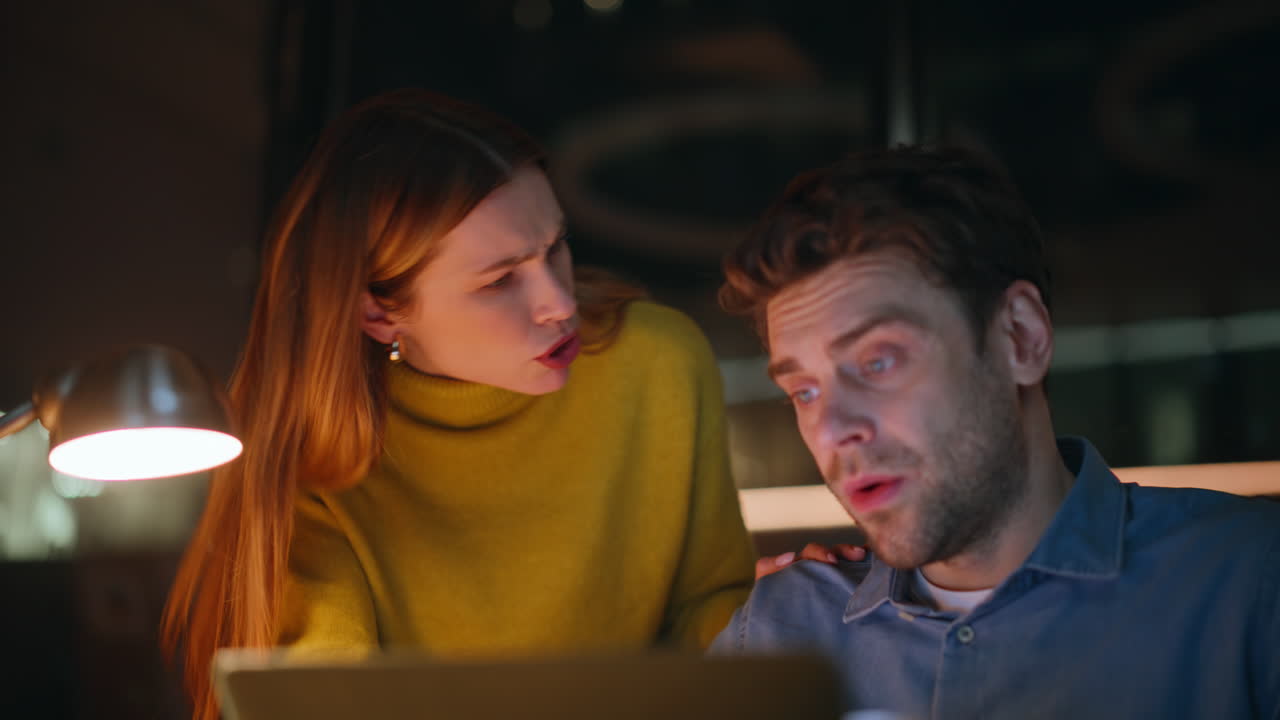 Late workers discussing project looking laptop screen at night office closeup