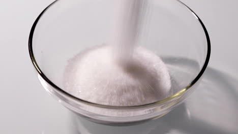 White-grains-of-sugar-being-poured-into-a-clear-glass-bowl