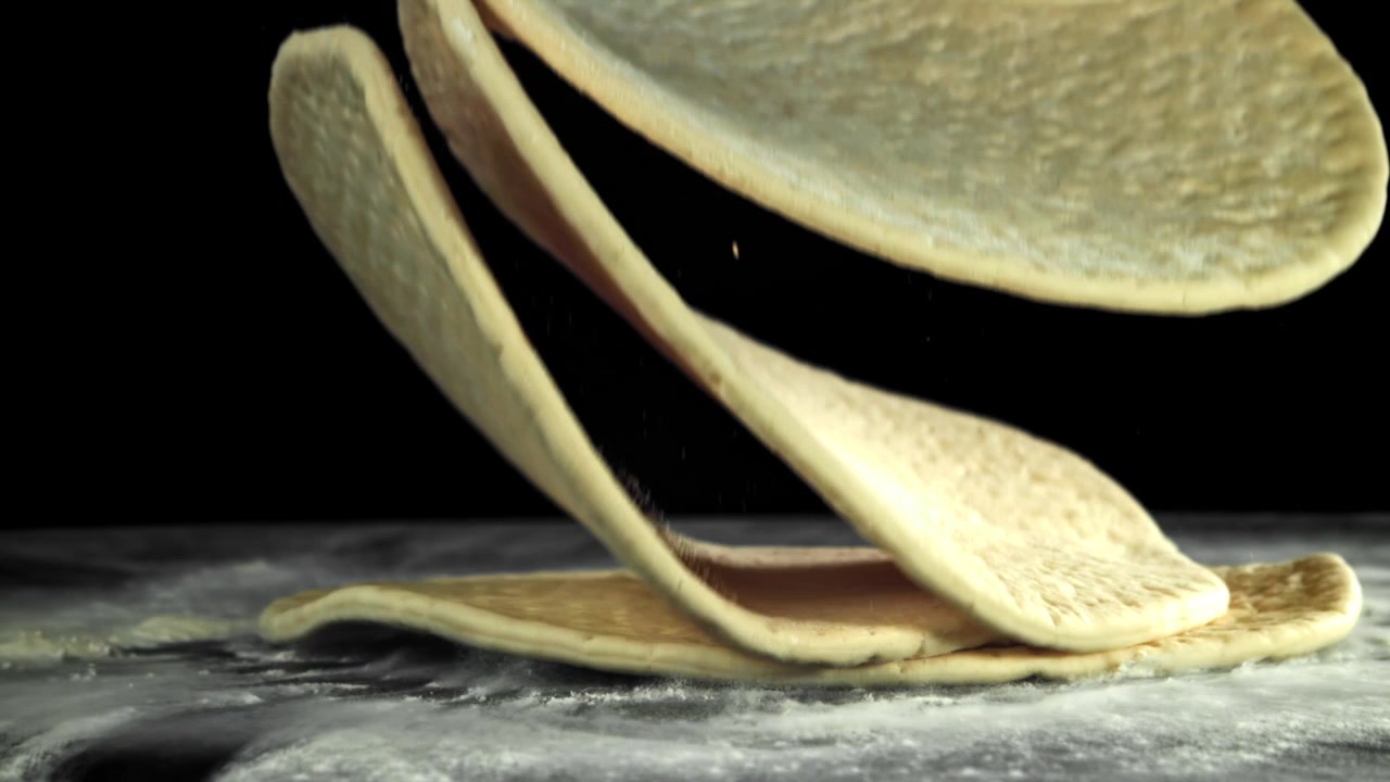 Fresh Pizza Doughs Falling onto a Floured Surface in Slow Motion