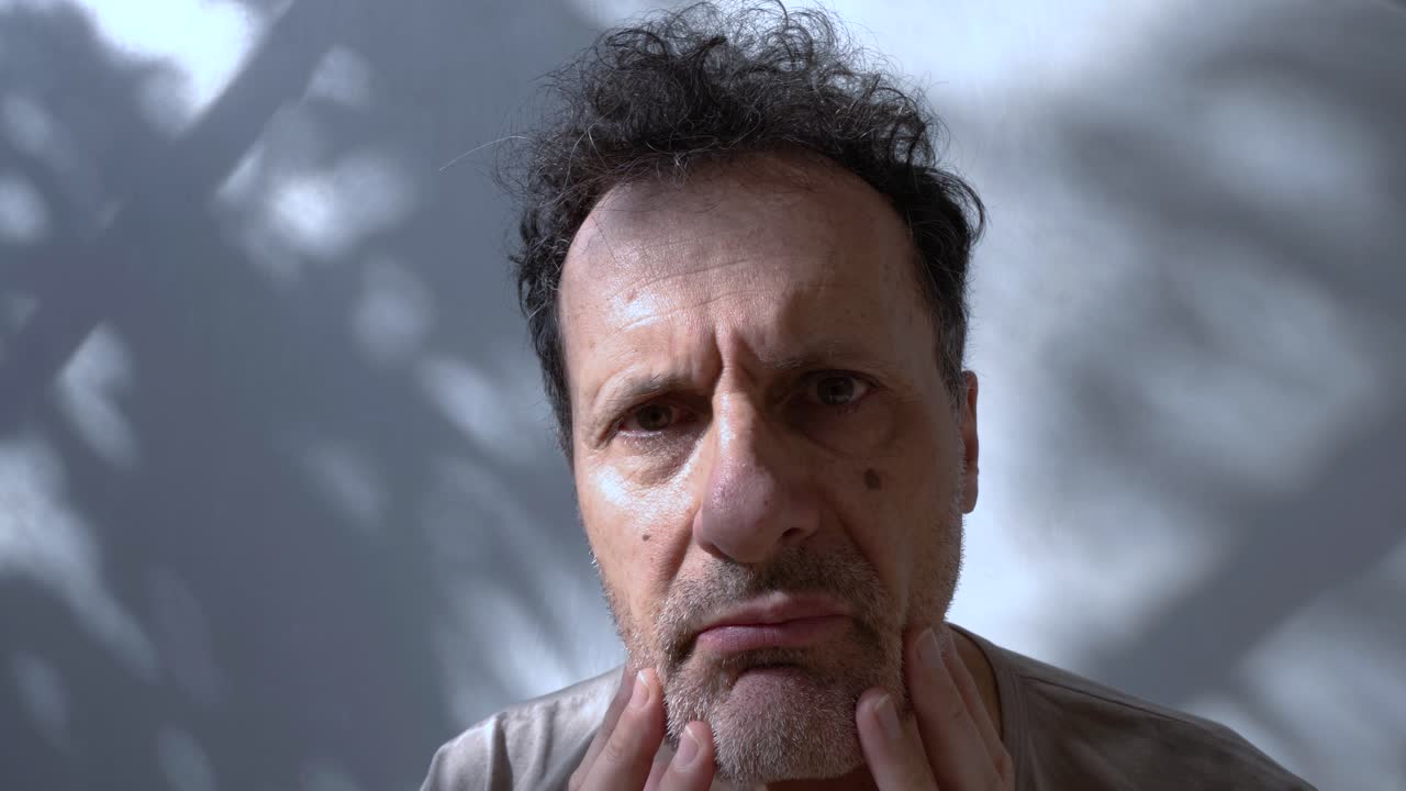 hombre capturado en un momento de ansiedad sosteniendo su cara, transmitiendo una profunda preocupación mirando a la cámara