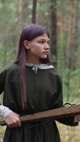 mädchen mit armbrust in der hand geht durch den wald und schaut sich um, antike, historische rekonstruktion