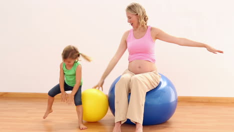 blonde pregnant woman sitting on exercise ball with her little girl