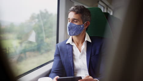 businessman on train using mobile phone wearing ppe face mask during health pandemic