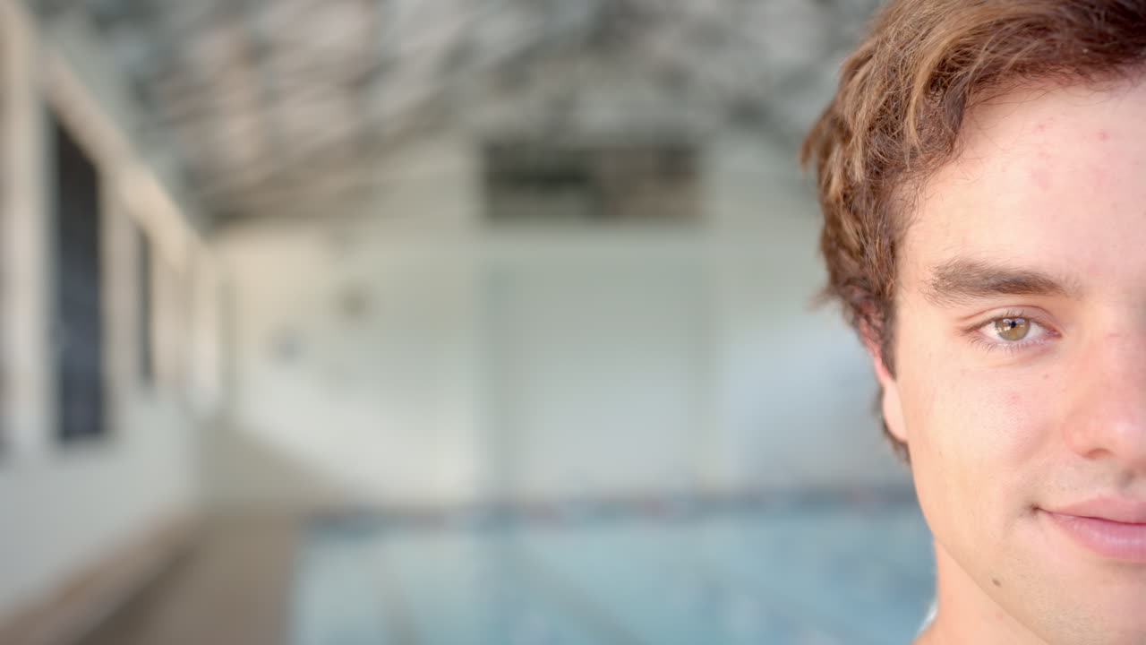 Close-up of male swimmer smiling, indoor pool in background, preparing for swim, copy space