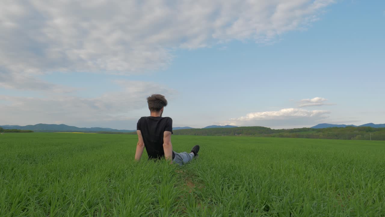 Young Caucasian Man Sitting on Green Grass Field Looking at Blue Sky