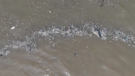 Low-altitude-ascending-top-down-drone-shot-of-polluted-water-filled-with-floating-trash-and-muddy-river-runoff-mixing-with-turqouise-tropical-water-of-Bali-Indonesia