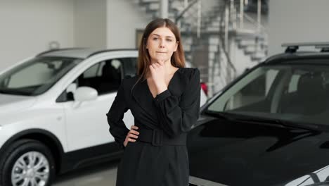 hermosa chica con un vestido negro se encuentra en un fondo de autos reflexionando sobre comprar un auto